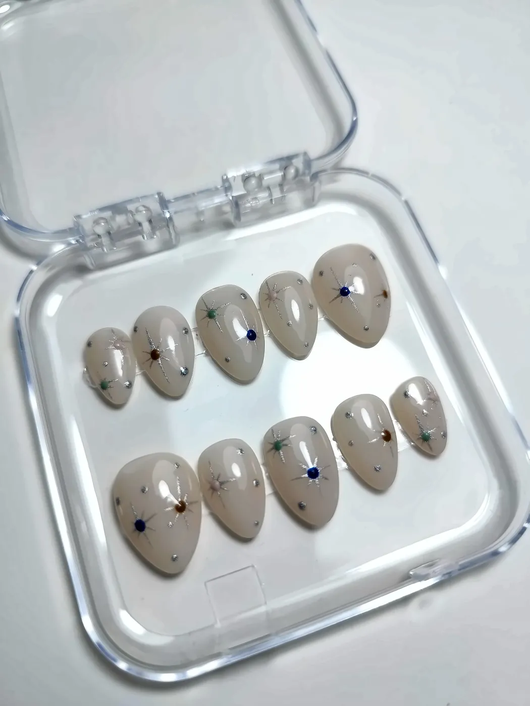 Uñas postizas almendra en blanco lechoso con estrellas y puntos plateados, en su cajita transparente