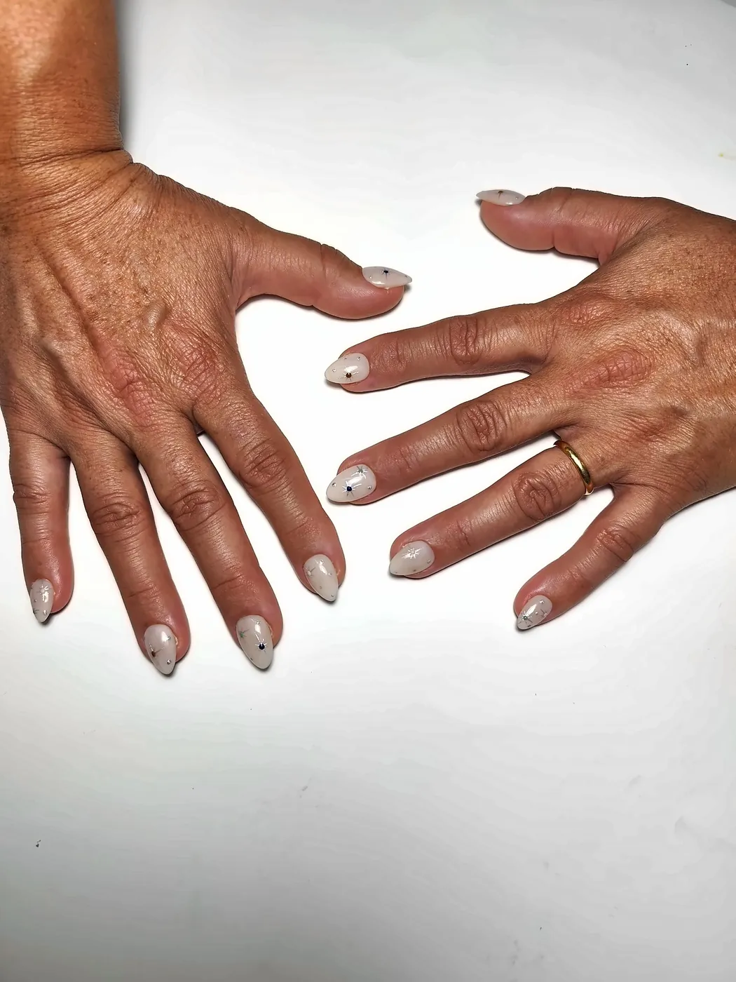 Dos manos abiertas con uñas postizas almendra en blanco lechoso con estrellas plateadas