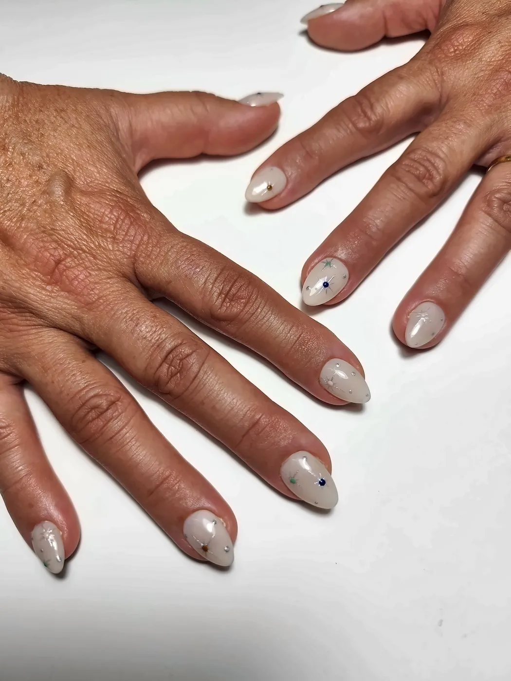 Mano con uñas postizas almendra en blanco lechoso con estrellas plateadas, de cerca