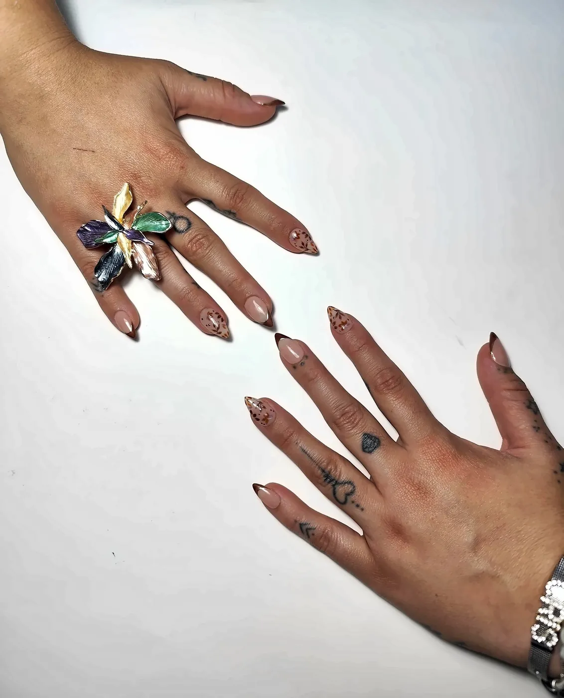 Dos manos abiertas con uñas postizas almendra con francesa marrón ojo de gato y hojas otoñales pintadas a mano