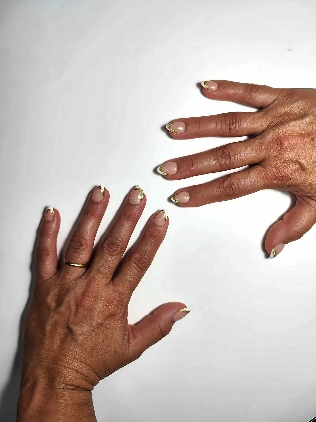 Dos manos abiertas con uñas postizas almendra cortas en nude con francesa blanca y línea dorada ondulada