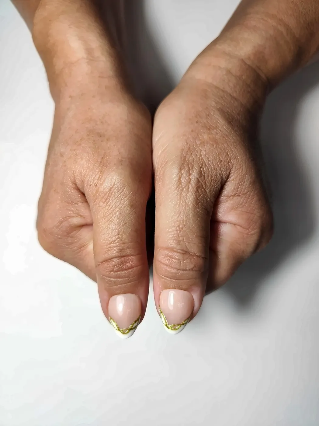 Primer plano de los pulgares con uñas postizas almendra en nude con francesa blanca y línea dorada ondulada