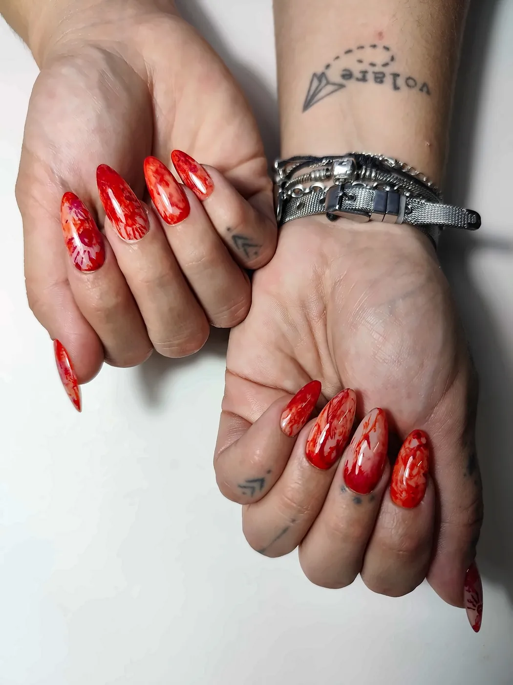 Dos manos con uñas postizas almendra largas en rojo acuarela con huellas de manos ensangrentadas
