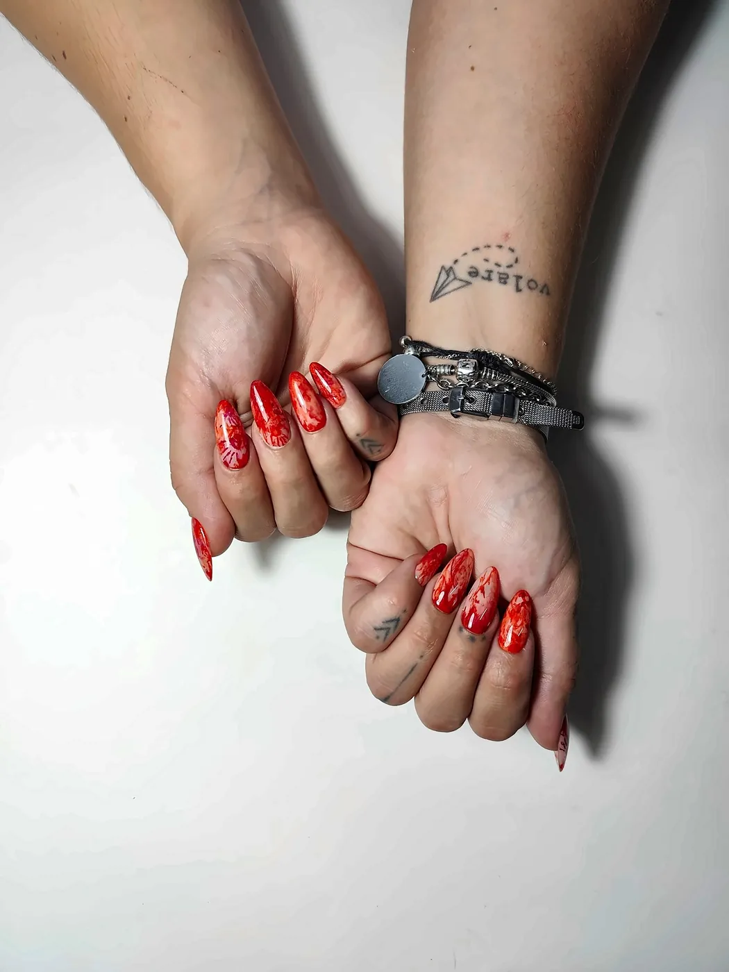 Manos cruzadas con uñas postizas almendra largas en rojo acuarela con huellas ensangrentadas