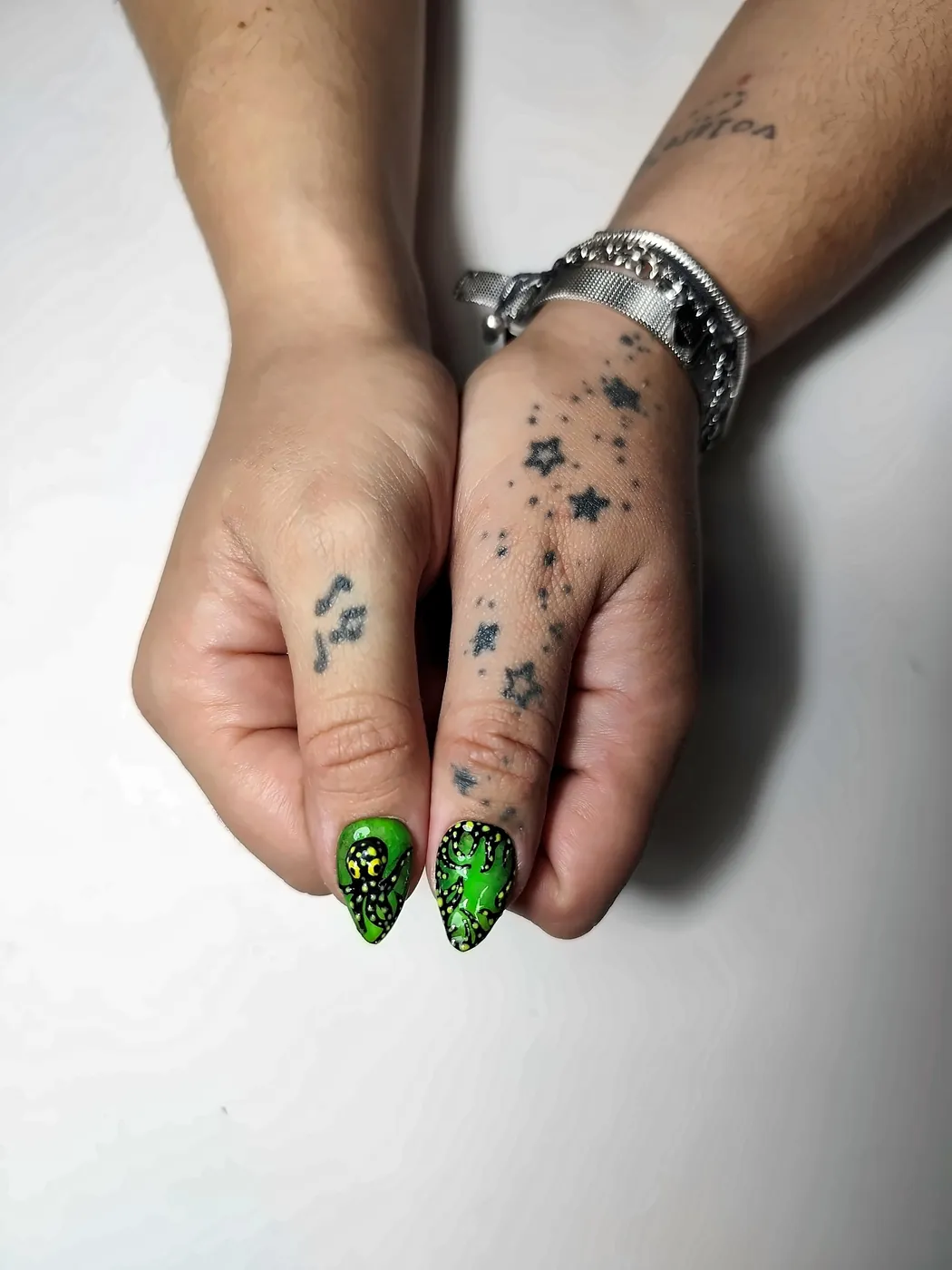 Primer plano de los pulgares con uñas postizas almendra en verde neón con un pulpo y tentáculos pintados a mano