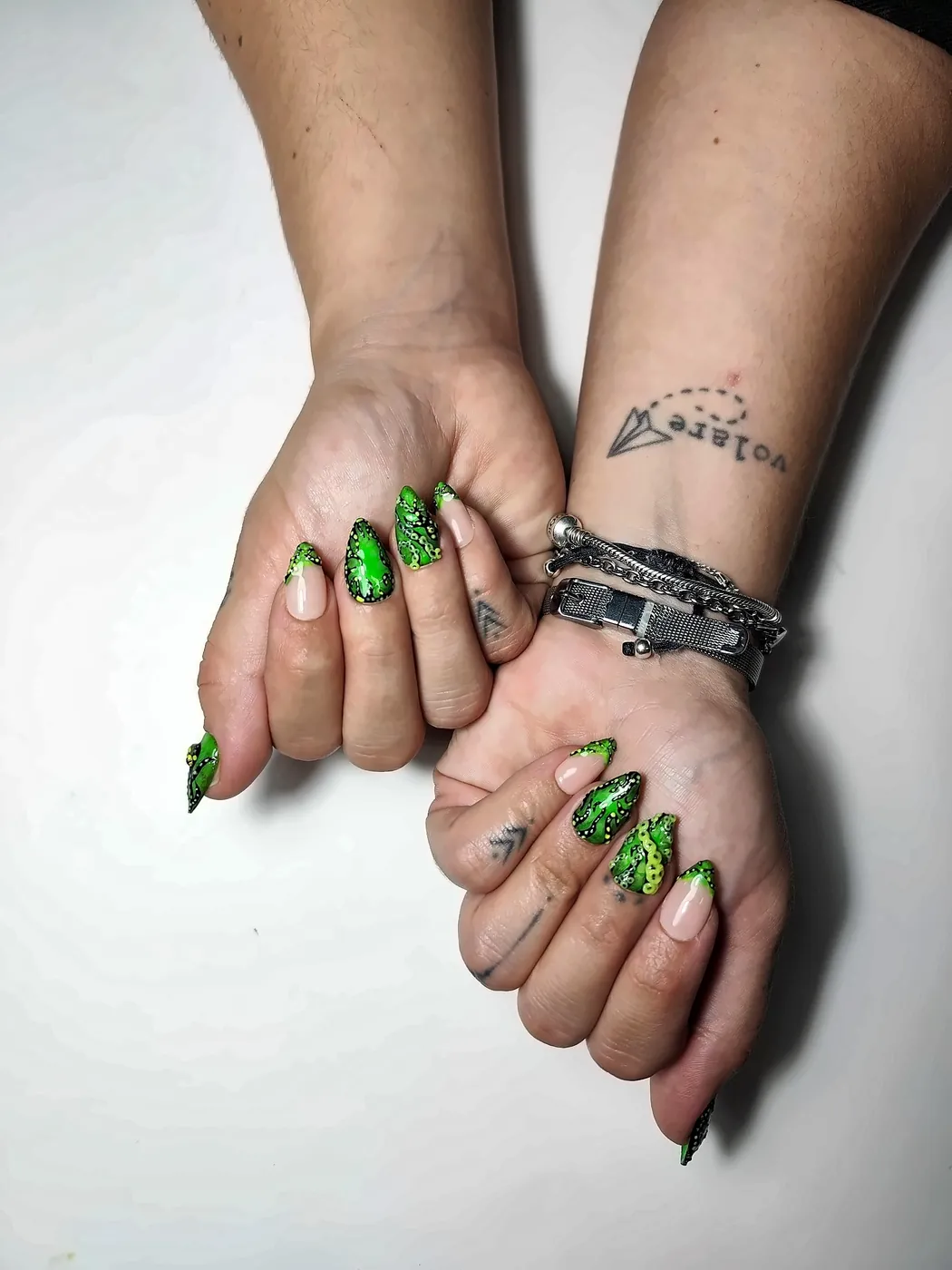 Manos cruzadas con uñas postizas almendra en verde neón con tentáculos de pulpo pintados a mano y francesas verdes