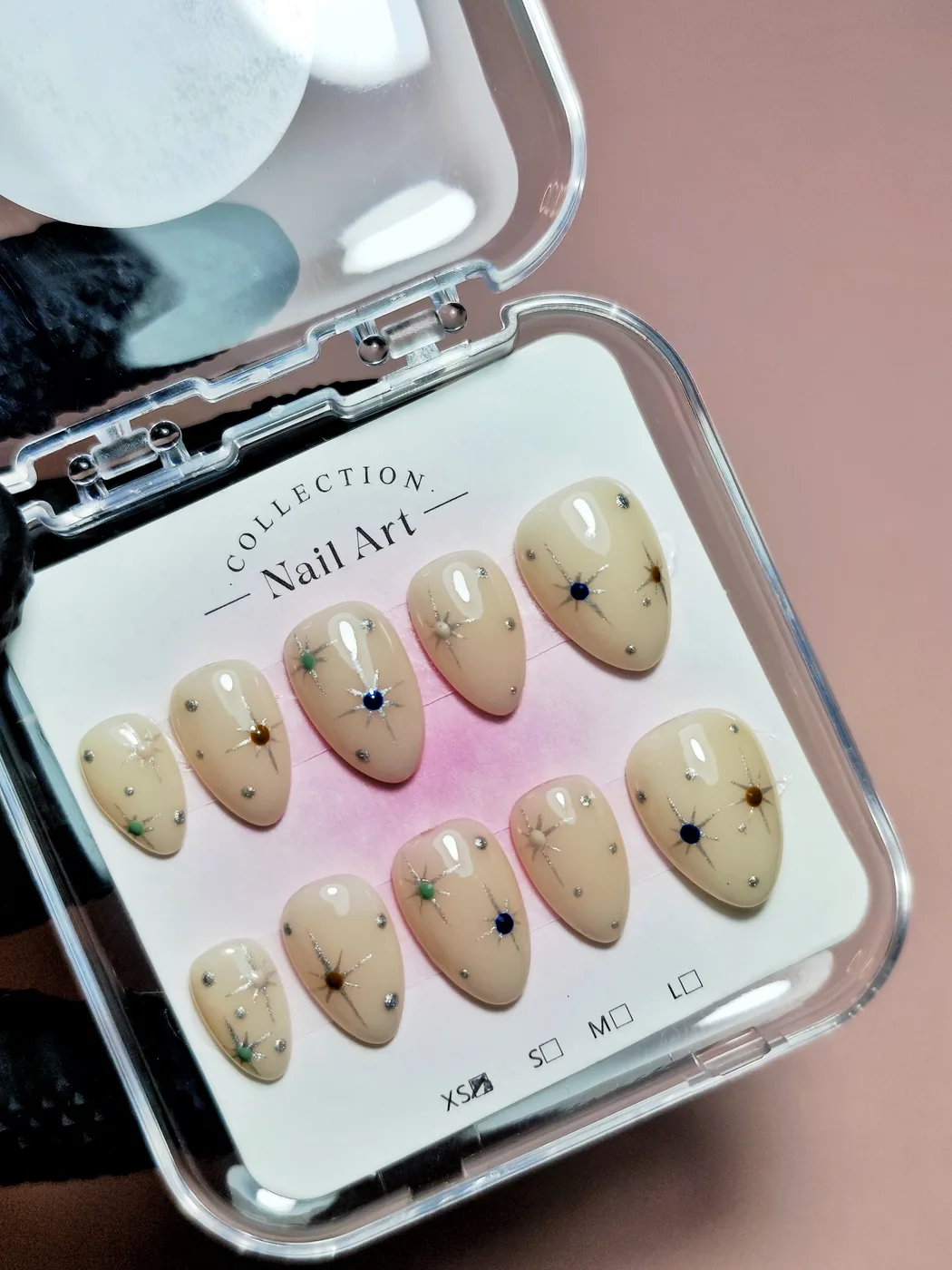 Set de uñas postizas almendra en su estuche, en nude crema con estrellas finas pintadas en varios colores y pedrería