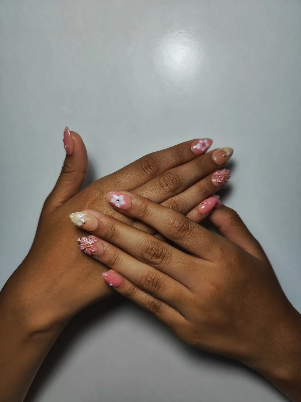 Dos manos con uñas postizas almendra cortas en nude rosado con florecitas blancas en relieve 3D y detalles en tonos pastel