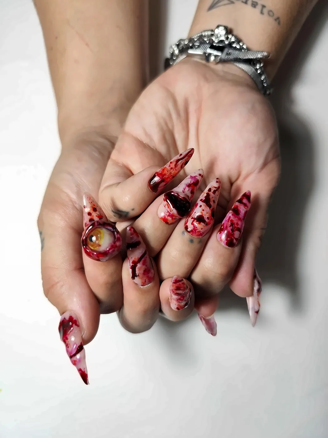 Manos juntas con uñas postizas stiletto con efecto sangre, heridas en relieve y ojo 3D