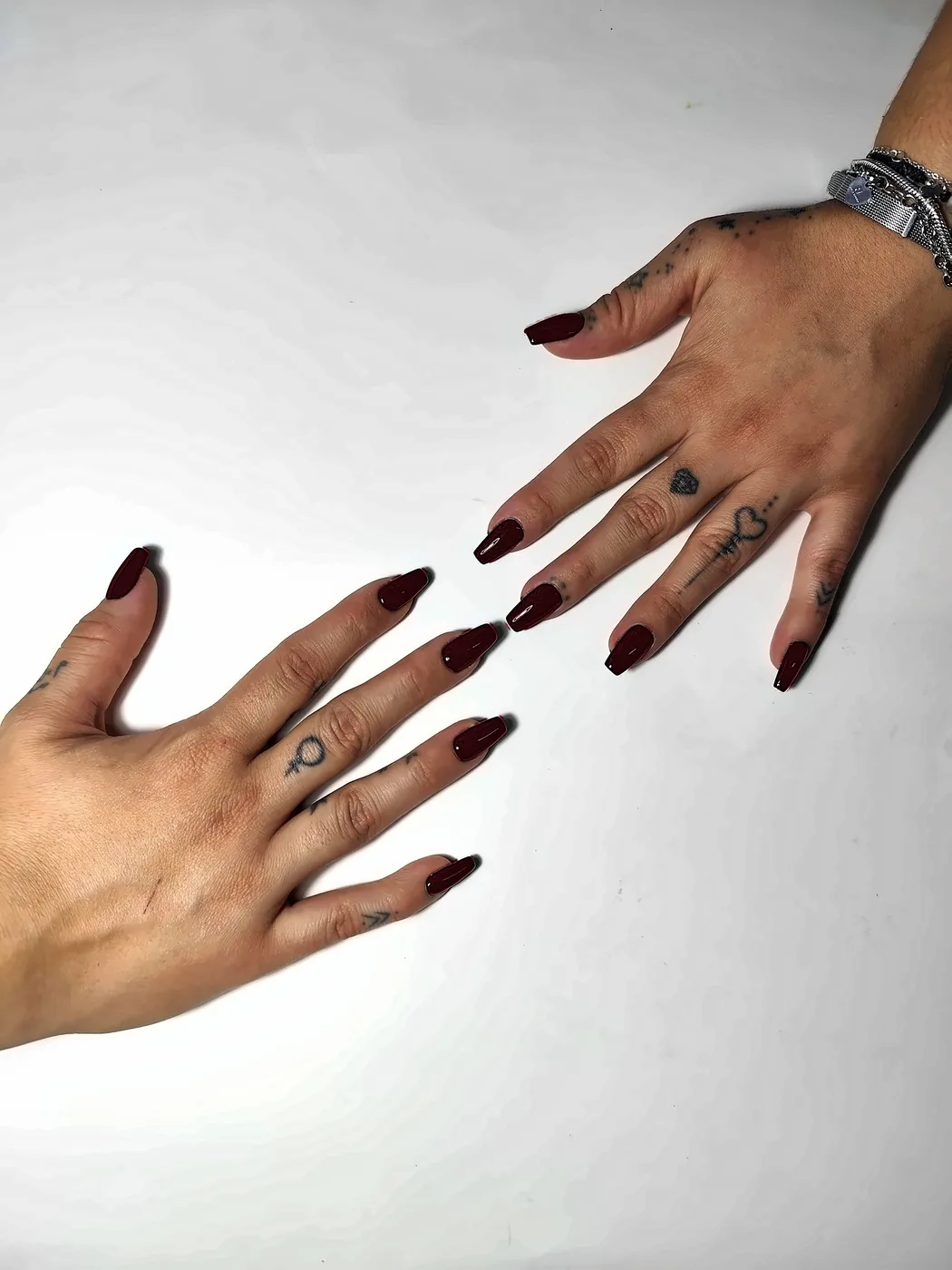 Dos manos que se acercan con uñas postizas coffin lisas en rojo vino, con acabado brillante