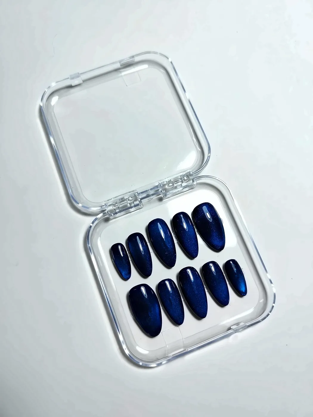 Uñas postizas almendra largas en azul marino con efecto ojo de gato, en su cajita transparente