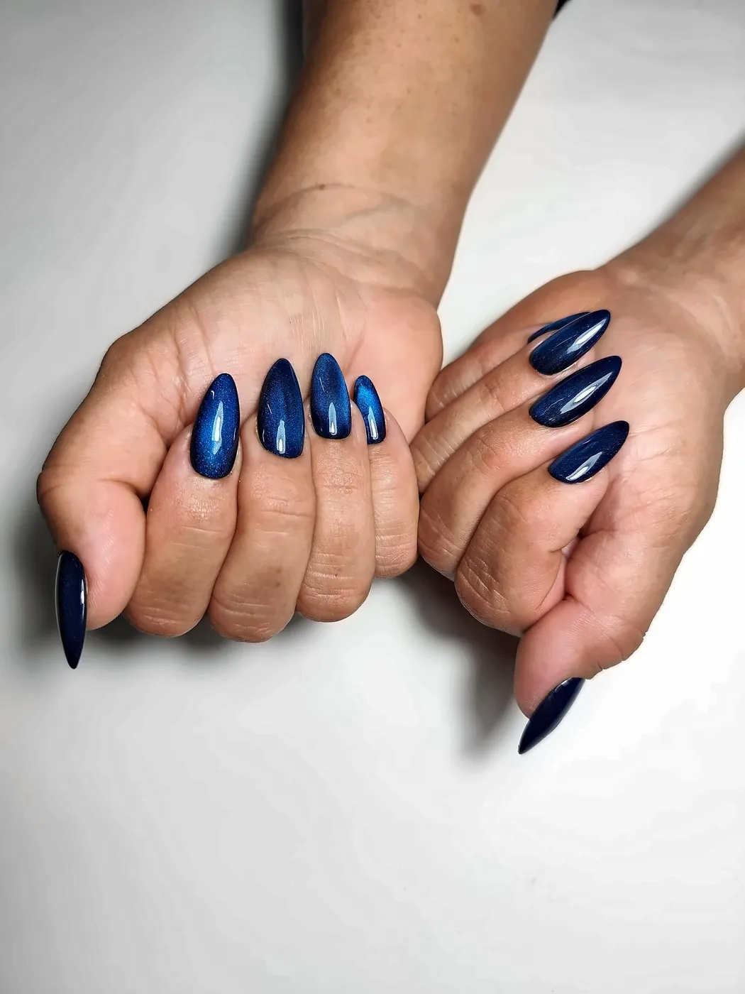 Manos juntas con uñas postizas almendra largas en azul marino con efecto ojo de gato
