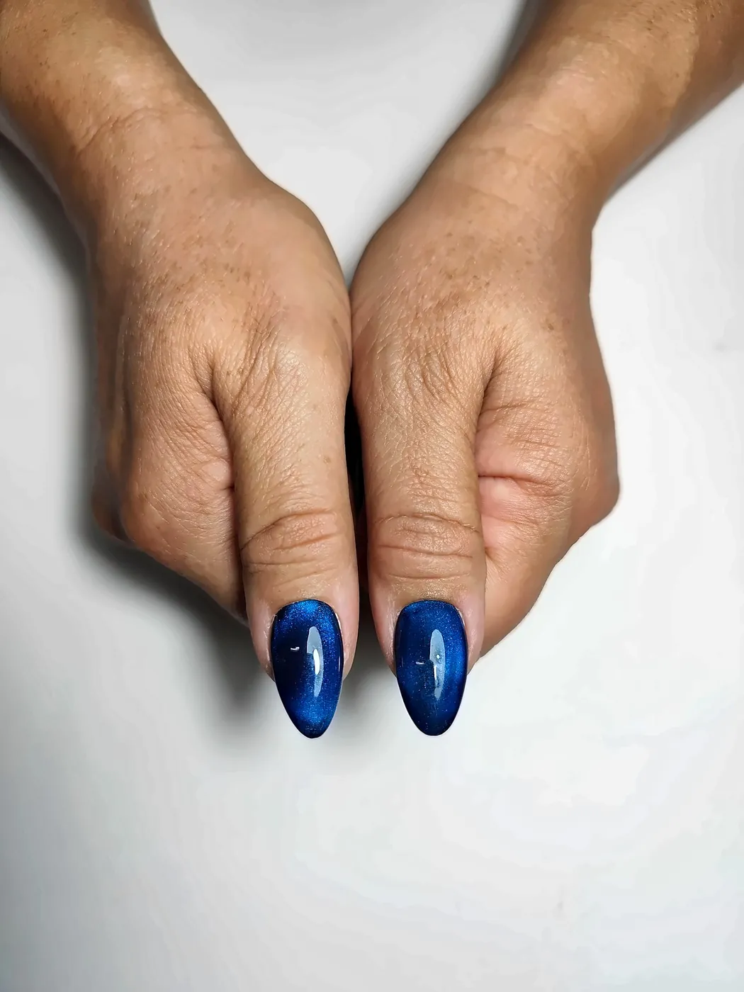 Primer plano de los pulgares con uñas postizas almendra en azul marino con efecto ojo de gato