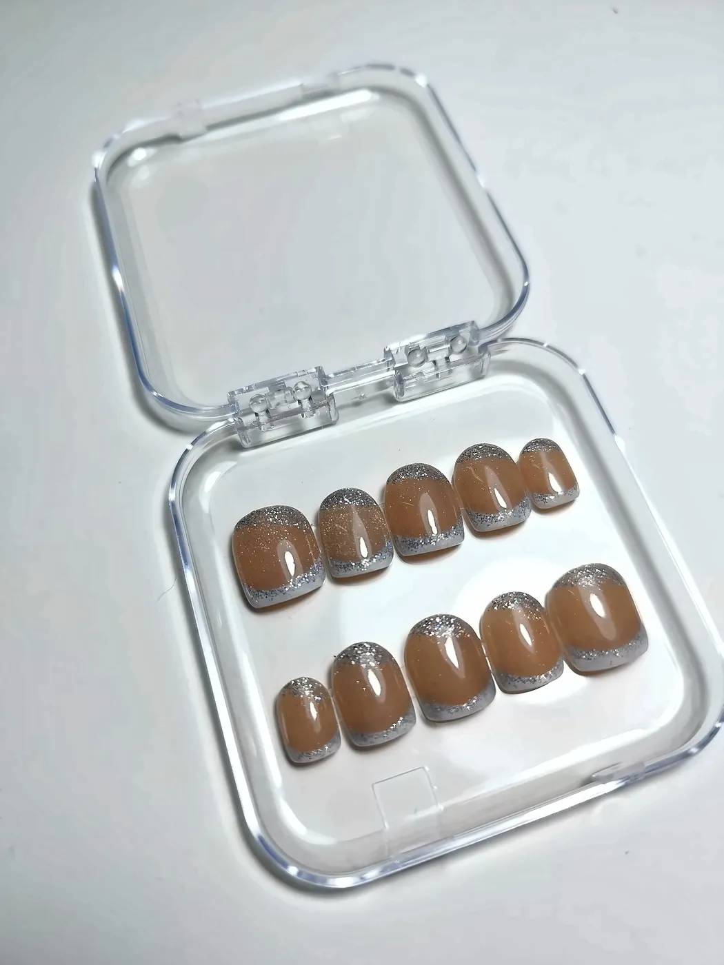 Uñas postizas squoval cortas en nude caramelo con francesa plateada con purpurina, en su cajita transparente