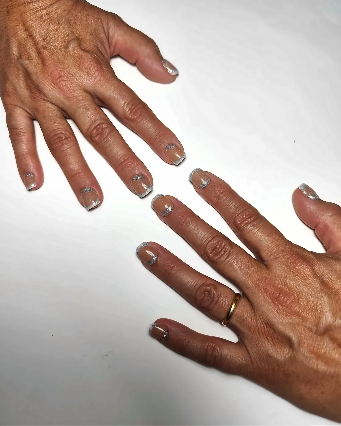 Dos manos abiertas con uñas postizas squoval cortas en nude caramelo con francesa plateada con purpurina