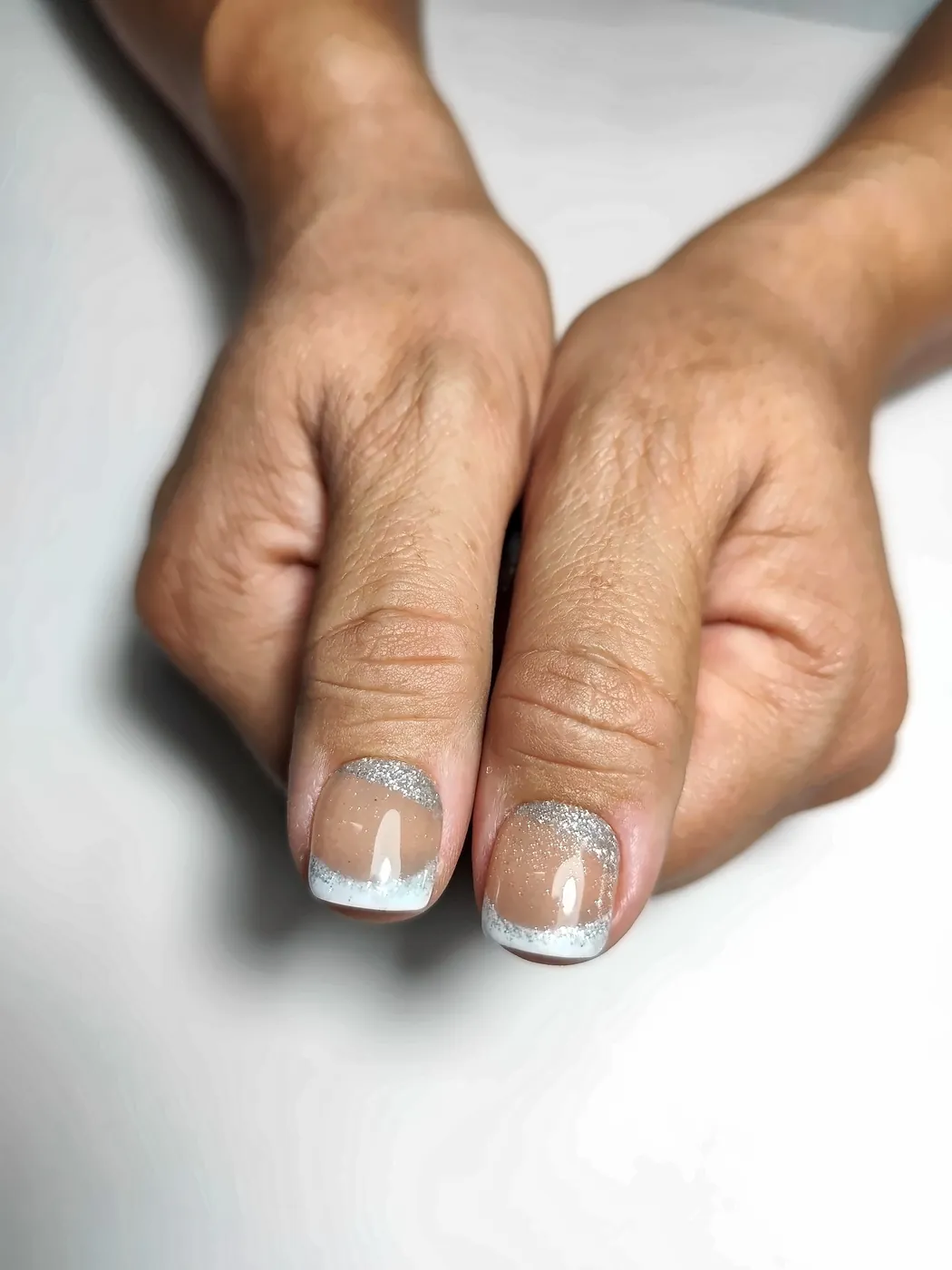 Primer plano de los pulgares con uñas postizas squoval en nude caramelo con francesa plateada con purpurina